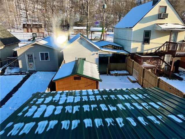 snow covered back of property featuring a wooden deck and a shed