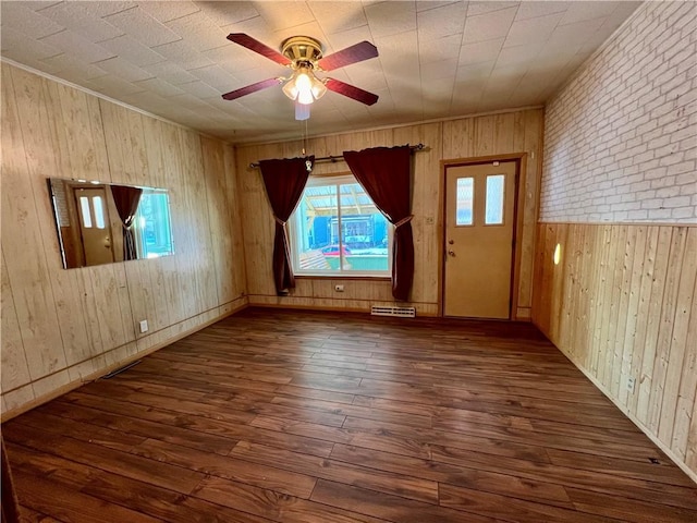 unfurnished room with ceiling fan, dark hardwood / wood-style flooring, brick wall, and wood walls