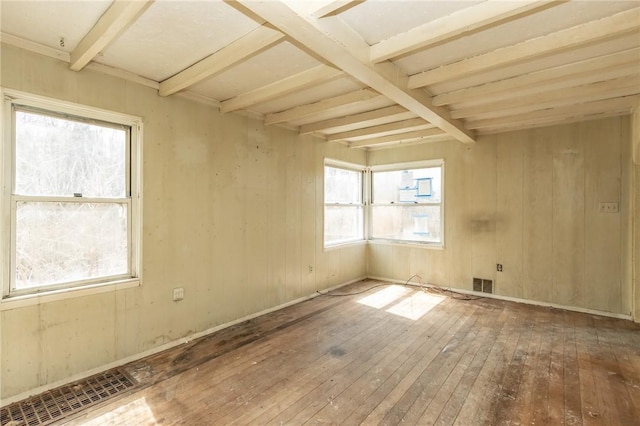spare room featuring wood-type flooring, a healthy amount of sunlight, beamed ceiling, and visible vents