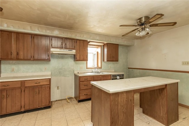 kitchen with light countertops, under cabinet range hood, a sink, ceiling fan, and brown cabinetry