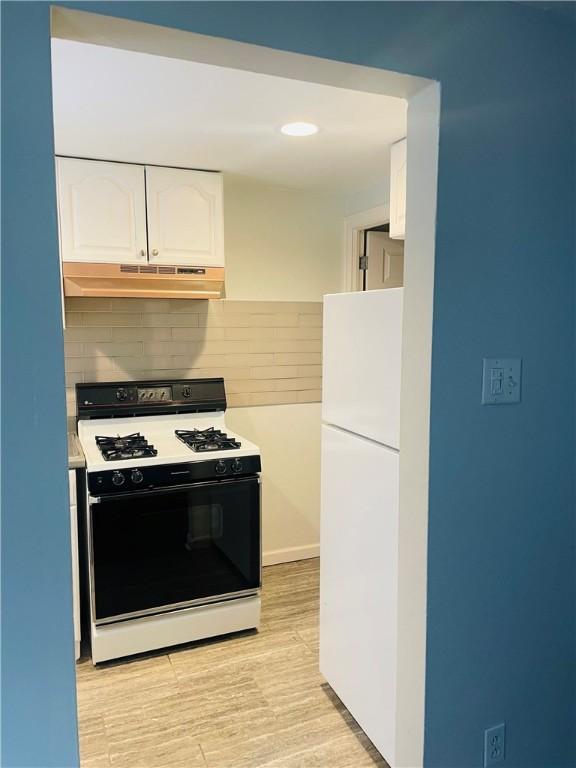 kitchen with light hardwood / wood-style floors, backsplash, gas range, white refrigerator, and white cabinets