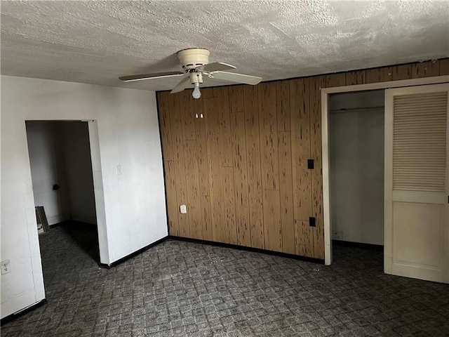 unfurnished bedroom with ceiling fan, a textured ceiling, a closet, and wooden walls