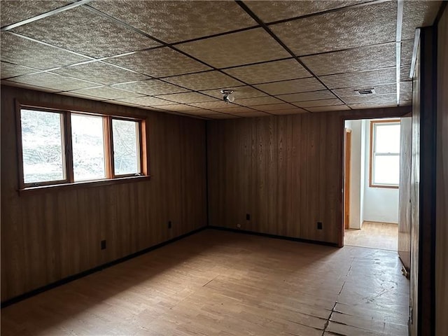 unfurnished room featuring a paneled ceiling, plenty of natural light, and wood walls