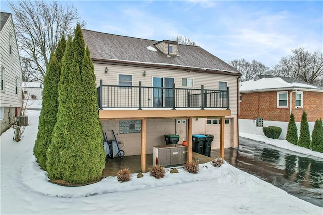 snow covered house featuring a garage, cooling unit, and a balcony