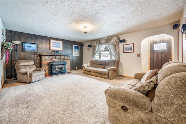 living room featuring a textured ceiling, wood walls, a wood stove, and carpet flooring