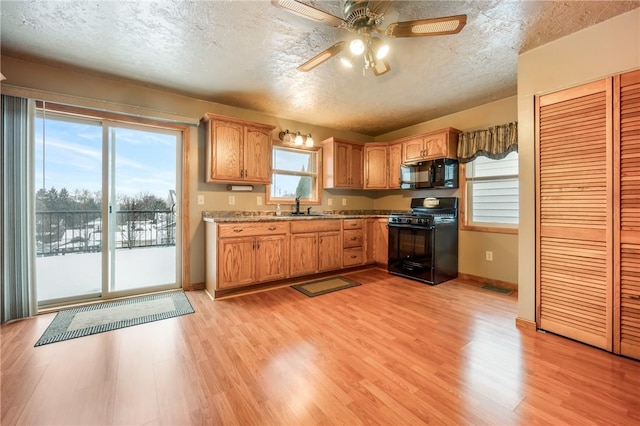 kitchen featuring black appliances, plenty of natural light, a textured ceiling, and light hardwood / wood-style flooring