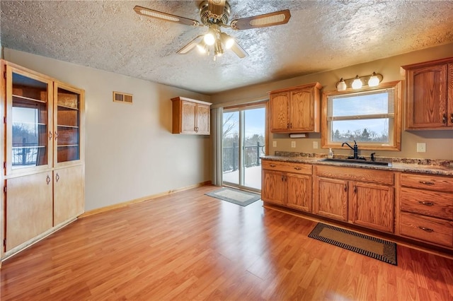 kitchen featuring light stone countertops, a textured ceiling, sink, ceiling fan, and light hardwood / wood-style flooring