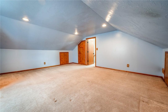 additional living space featuring light colored carpet, vaulted ceiling, and a textured ceiling