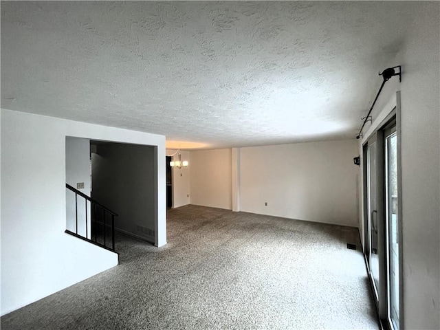 carpeted spare room with a textured ceiling and a chandelier