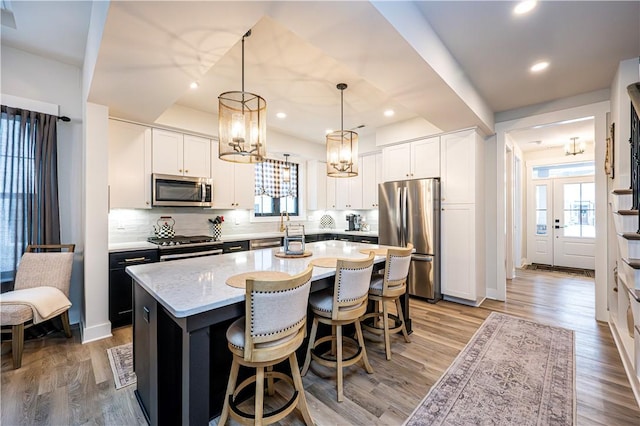 kitchen with a kitchen island with sink, decorative backsplash, stainless steel appliances, and white cabinets