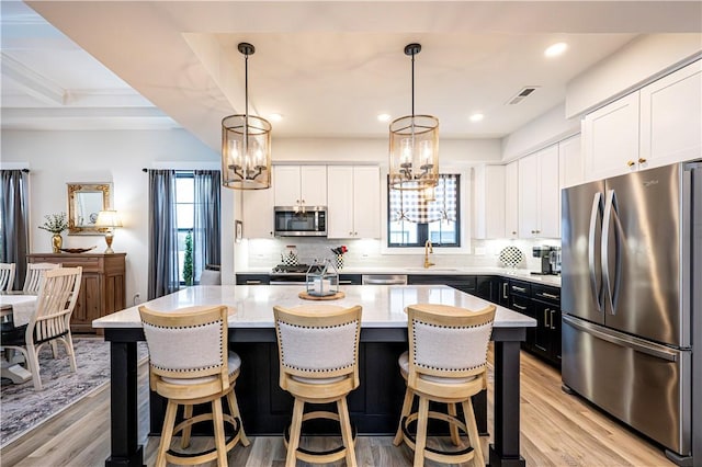 kitchen with pendant lighting, stainless steel appliances, white cabinets, and a kitchen island