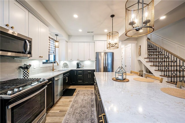 kitchen featuring white cabinetry, stainless steel appliances, light stone countertops, light hardwood / wood-style floors, and decorative light fixtures