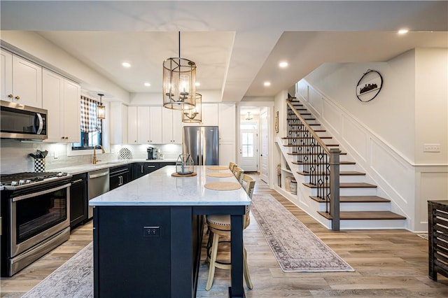 kitchen featuring pendant lighting, stainless steel appliances, a center island, light stone counters, and light hardwood / wood-style floors