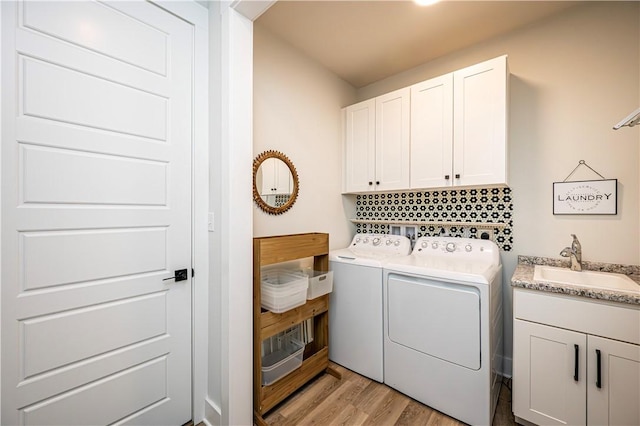 clothes washing area with cabinets, washing machine and dryer, sink, and light wood-type flooring