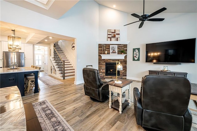 living room featuring ceiling fan with notable chandelier, high vaulted ceiling, a fireplace, and light hardwood / wood-style floors