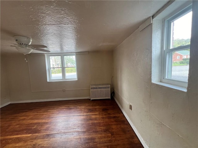 empty room featuring dark hardwood / wood-style flooring, a wealth of natural light, radiator heating unit, and a textured ceiling