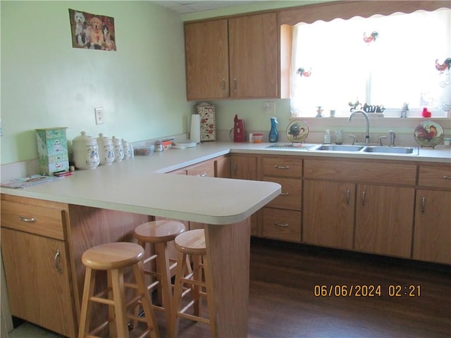 kitchen with kitchen peninsula, dark wood-type flooring, sink, and a breakfast bar area