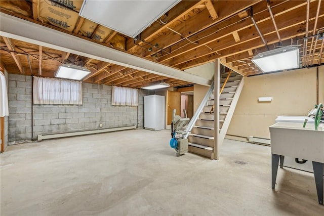 basement featuring a baseboard heating unit, white refrigerator, and sink