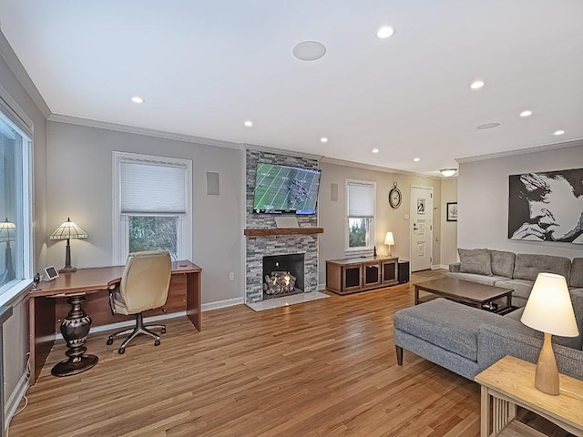 living room with light wood-type flooring, ornamental molding, and a stone fireplace