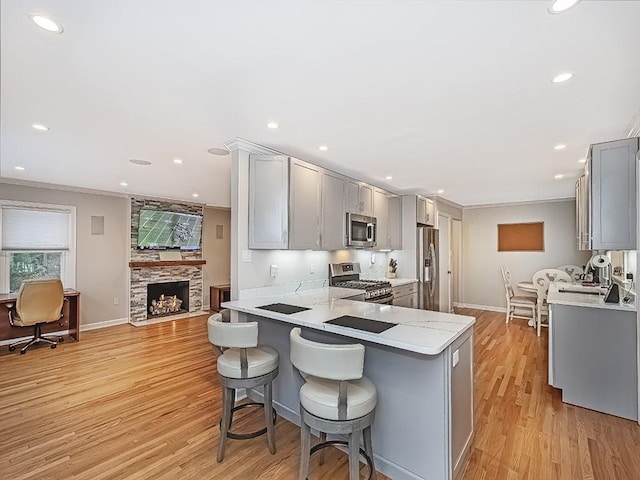 kitchen featuring kitchen peninsula, light wood-type flooring, light stone countertops, appliances with stainless steel finishes, and gray cabinetry