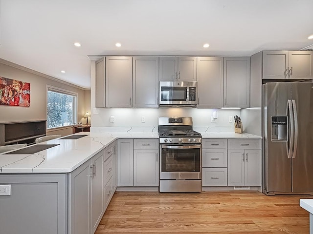 kitchen with light stone countertops, appliances with stainless steel finishes, gray cabinetry, and light hardwood / wood-style flooring