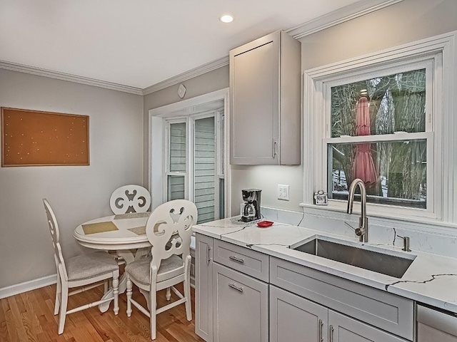 kitchen with gray cabinets, crown molding, light hardwood / wood-style flooring, light stone counters, and sink