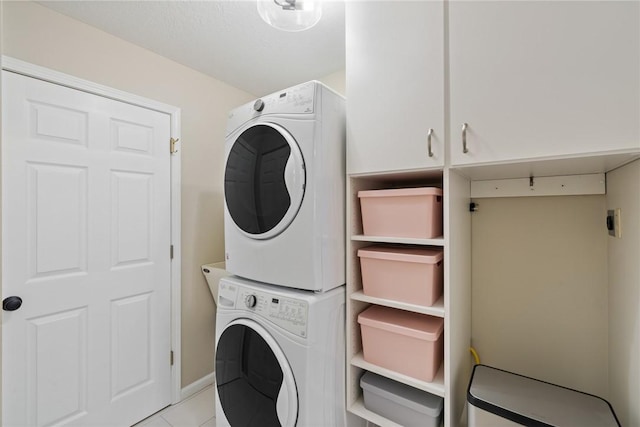 laundry room with cabinets, light tile patterned flooring, and stacked washer / dryer