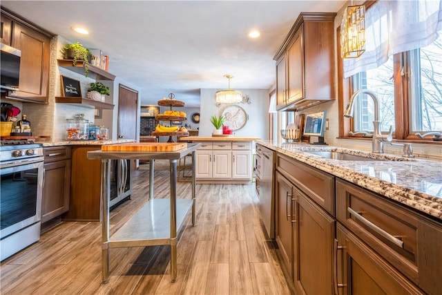 kitchen with appliances with stainless steel finishes, sink, hanging light fixtures, a notable chandelier, and light hardwood / wood-style flooring