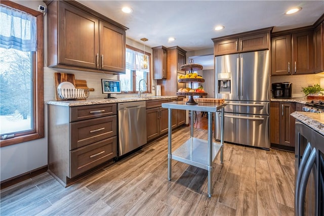 kitchen with hardwood / wood-style floors, stainless steel appliances, tasteful backsplash, pendant lighting, and light stone counters