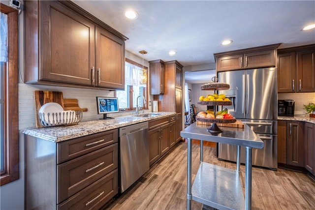 kitchen with backsplash, pendant lighting, sink, light wood-type flooring, and appliances with stainless steel finishes