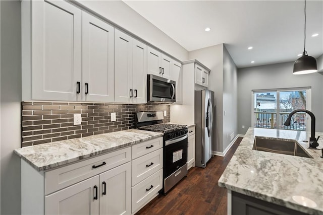 kitchen featuring appliances with stainless steel finishes, pendant lighting, white cabinets, light stone counters, and sink