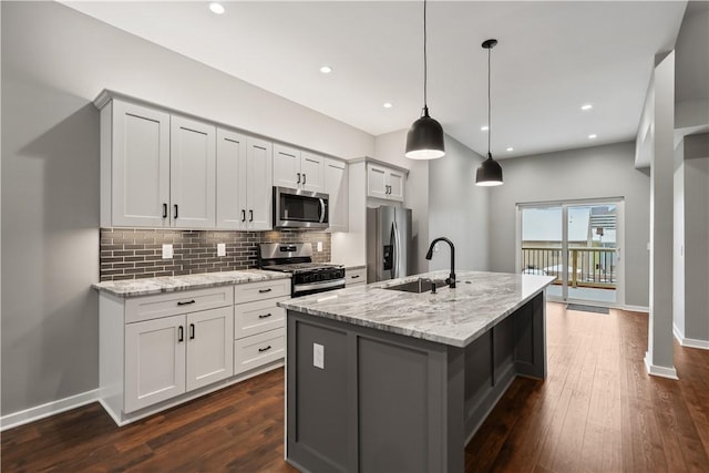 kitchen with stainless steel appliances, an island with sink, sink, hanging light fixtures, and light stone counters