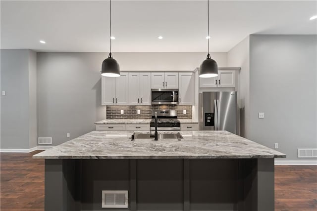 kitchen with a center island with sink, appliances with stainless steel finishes, light stone counters, and hanging light fixtures