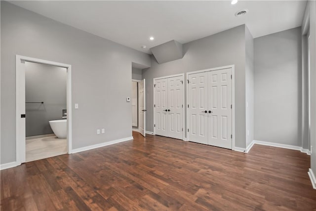 unfurnished bedroom with ensuite bath, multiple closets, and dark hardwood / wood-style floors