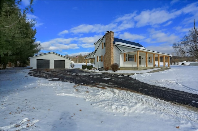 view of snow covered exterior featuring a garage, an outdoor structure, and a porch