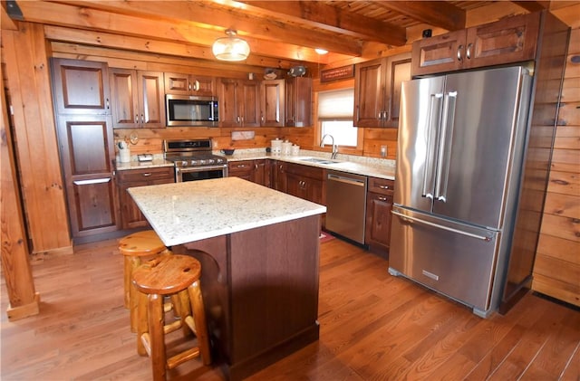 kitchen featuring beam ceiling, appliances with stainless steel finishes, wood walls, and a center island