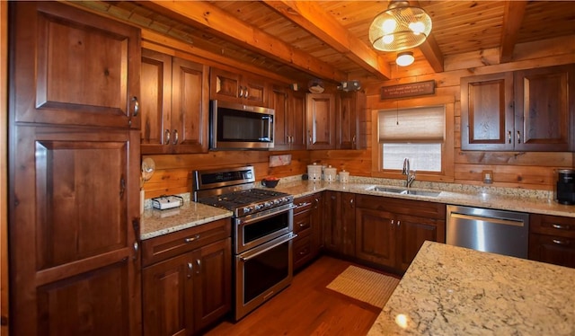 kitchen featuring stainless steel appliances, sink, hanging light fixtures, light stone counters, and beam ceiling