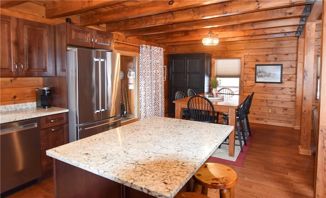 kitchen featuring wood walls, stainless steel appliances, light stone countertops, beam ceiling, and a center island