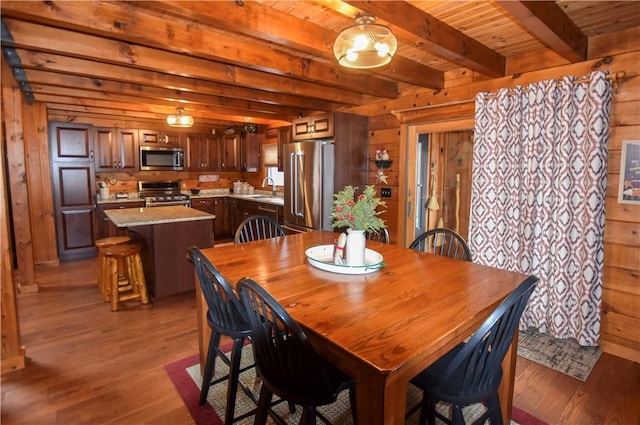 dining space with sink, dark hardwood / wood-style floors, beamed ceiling, and wooden walls