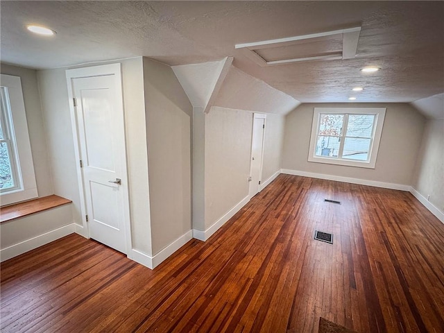 additional living space with vaulted ceiling, dark wood-type flooring, and a textured ceiling