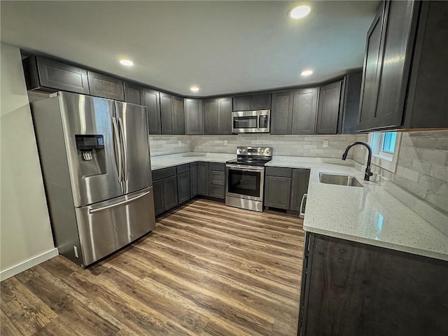 kitchen featuring tasteful backsplash, sink, stainless steel appliances, dark hardwood / wood-style flooring, and light stone counters