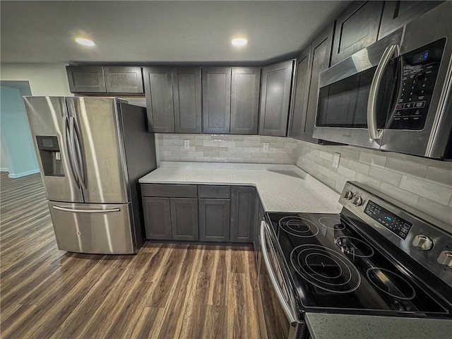 kitchen featuring dark hardwood / wood-style floors, appliances with stainless steel finishes, tasteful backsplash, and light stone counters