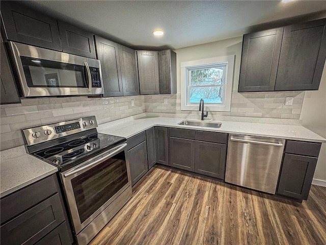 kitchen with appliances with stainless steel finishes, dark wood-type flooring, light stone counters, dark brown cabinetry, and sink