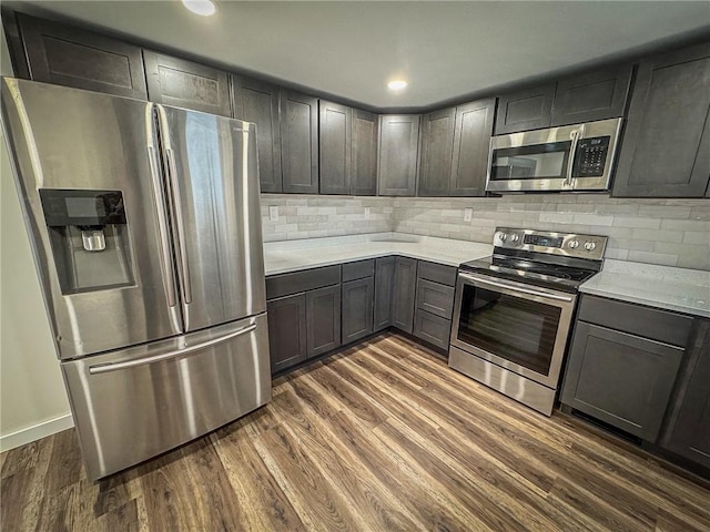 kitchen with appliances with stainless steel finishes, dark hardwood / wood-style floors, and tasteful backsplash