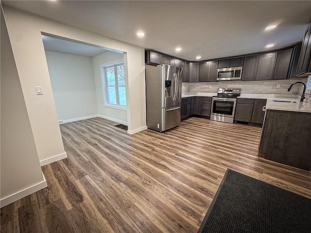 kitchen featuring hardwood / wood-style flooring, appliances with stainless steel finishes, decorative backsplash, dark brown cabinets, and sink