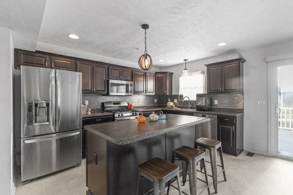 kitchen featuring tasteful backsplash, a center island, dark brown cabinets, appliances with stainless steel finishes, and pendant lighting