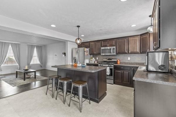 kitchen featuring a kitchen bar, a center island, dark brown cabinets, appliances with stainless steel finishes, and pendant lighting