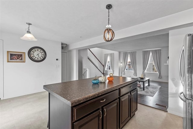 kitchen with pendant lighting, stainless steel refrigerator, dark brown cabinetry, a textured ceiling, and a kitchen island