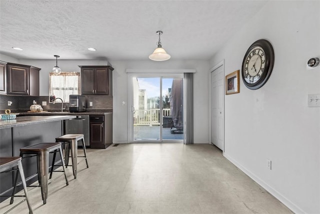 kitchen featuring pendant lighting, dark brown cabinetry, dishwasher, and a breakfast bar area