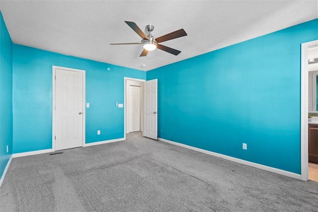 unfurnished bedroom with ensuite bath, carpet floors, and ceiling fan